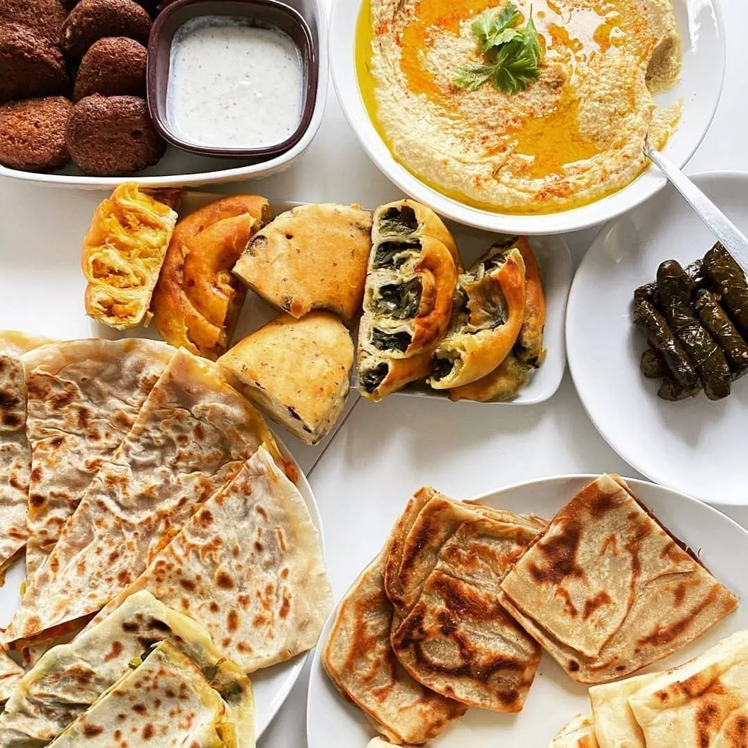 Table de brunch méditerranéen composée de houmous à l’huile d’olive, falafels, börek aux épinards, galettes grillées et dolmas